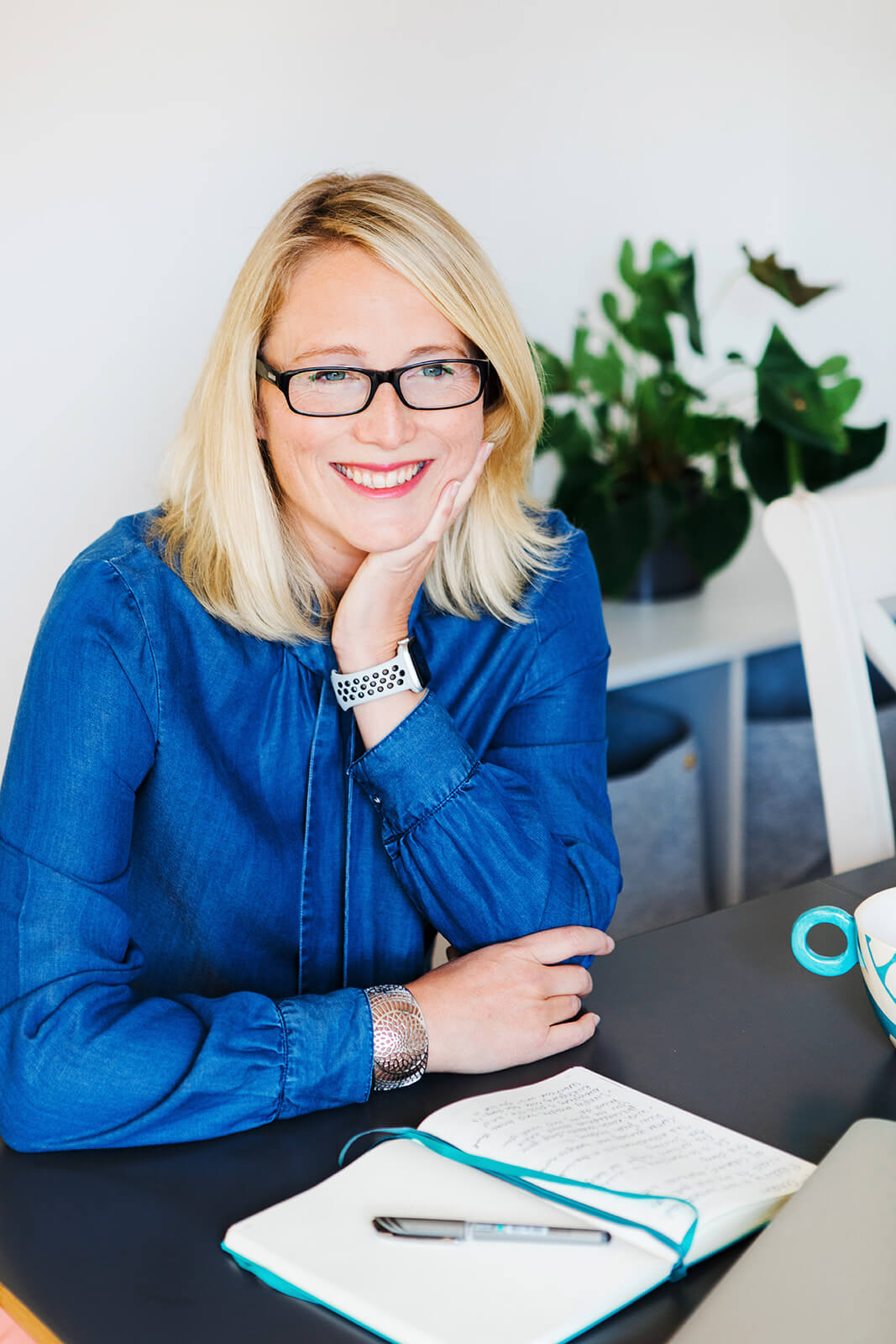 Portrait of Hazel Anderson Turner smiling at her desk with a notebook, featured in her article about overcoming imposter syndrome.